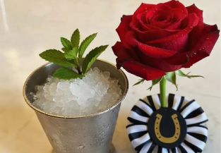 Mint julep cocktail with fresh mint beside a red rose and derby ribbon.